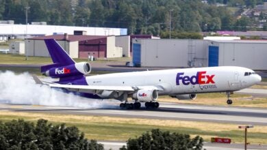 White smoke from the tires of a white/purple FedEx as it makes a hard landing on a runway.