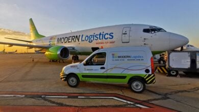 A van parked in front of a cargo jet, both in white and lime green colors of Modern Logistics as dawn sun creeps up.