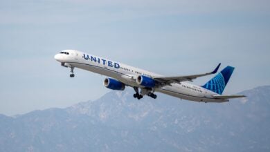 A blue-tailed United Airlines jet takes off with desert mountains in the background.