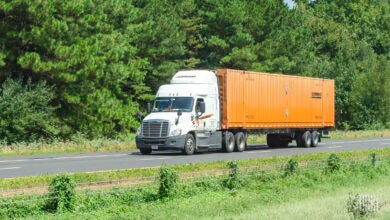 A Schneider tractor pulling an orange Schneider intermodal container on the highway