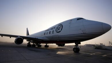 A close up side view of a white jumbo jet freighter, parked, with the morning sun glowing in the background.