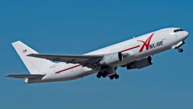 A large white jet with red ABX Air logo tilted in the sky as it comes in for a landing with wheels down.