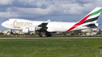 An Emirates SkyCargo jet with multi-colored tail lands on runway.