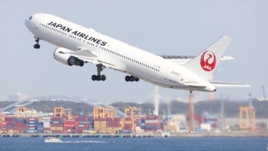 A white Japan Airlines jet with red lettering takes off from an airport.