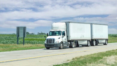 A white day cab pulling two white LTL trailers on highway