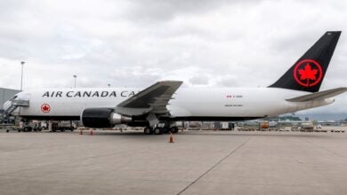 An Air Canada Cargo jet with black tail and red maple leaf logo parked at an airport. Viewed from the side.