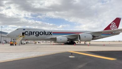 Side view of a jumbo jet freighter with a red tail and Cargolux logo on the airport parking area.