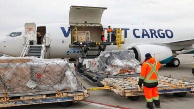 A man in an orange work outfit oversees the loading of pallets through the side door of a WestJet Cargo plane.