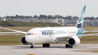 A jet with teal accents and WestJet logo rolls on a runway.