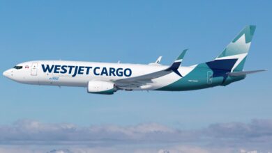 A WestJet Cargo plane with teal tail flies across blue sky.