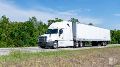 A white tractor pulling a white trailer on a highway