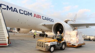 A tug pulls a pallet of cargo next to a CMA CGM Air Cargo freighter.