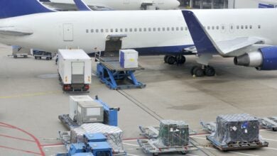 Cargo containers scattered on the ramp next to a white passenger airliner with blue accents.