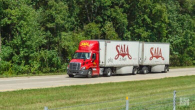 A red Saia tractor pulling two white Saia trailers on a highway