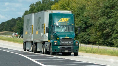 A green ABF tractor pulling two LTL trailers