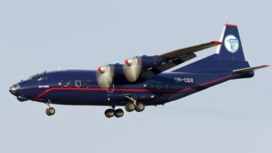 A dark blue four-engine propeller plane on approach with wheels down.