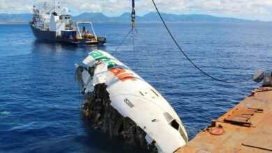 A crane lifts a section of a crashed plane from the ocean and gets ready to place it on a barge.