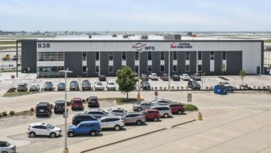 A large building with the WFS and China Airlines logos, cars parked in the lot and aircraft in the background on a sunny day.