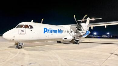 A small propeller plane in the Amazon Prime Air logo on the tarmac at night.