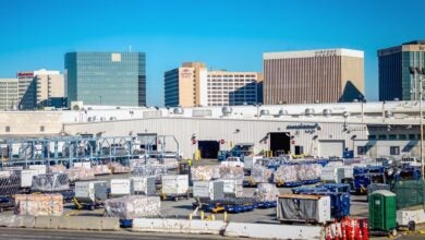 Air cargo containers on the tarmac at Los Angeles airport, with hotels in the background.