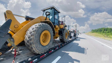 A tractor pulling a flatebed trailer with a wheel loader