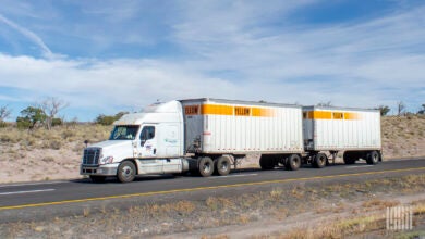 a white YRC Freight tractor pulling two Yellow LTL trailers