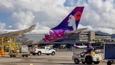 Purple and red tail on Hawaiian Airlines plane with equipment around it on tarmac.