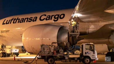 A close up photo of a Lufthansa Cargo jet being refueled at night be a tank truck.