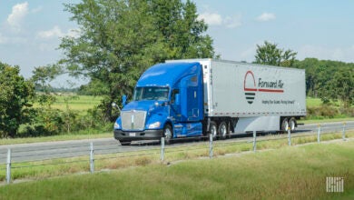 A blue tractor pulling a white Forward Air trailer on the road