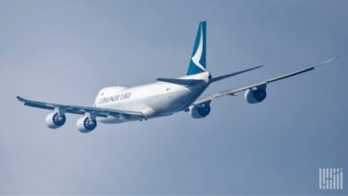 A Cathay Pacific cargo plane with teal tail flies high in sky away from camera.