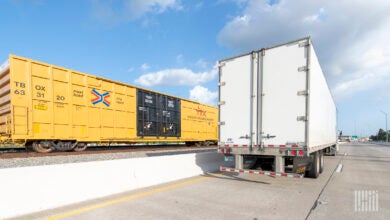 A tractor-trailer on a highaway next to a boxcar on a railroad