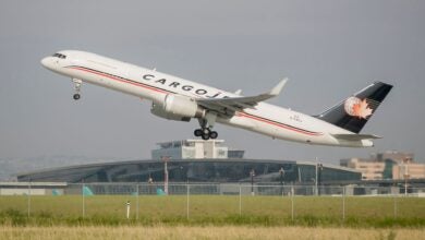 A white jet with blue tail labeled Cargojet takes off with airport terminal in the background.