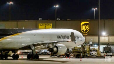 Night view of a brown-white UPS plane with the UPS logo on the cargo terminal next to it.