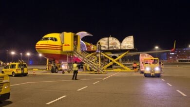 A mustard-colored DHL cargo plane being loaded at night.