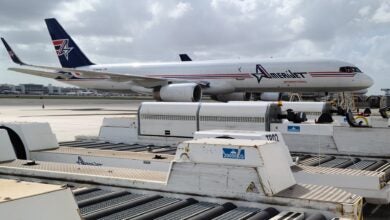 A blue-tailed Amerijet cargo plane on the tarmac next to roller beds.