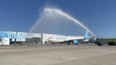 A fire truck shoots a spray of water over an Amazon Prime Air cargo jet to celebrate its first flight.