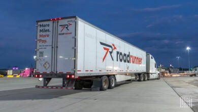 A white tractor pulling a white Roadrunner trailer at a truck stop