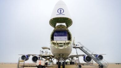 A giant freighter with its nose cone flipped open showing large cargo pallets on the main deck.