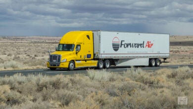 A Yellow tractor pulling a white Forward Air dry van trailer on a highway