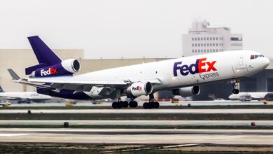 A purple-tail FedEx cargo jet takes off with buildings in the background.