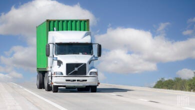 A white tractor hauling a green ocean container