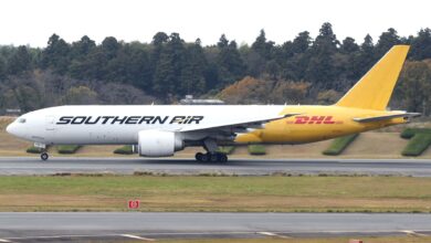 A yellow-tailed Southern Air/DHL freighter jet on the runway with evergreen trees in the background.