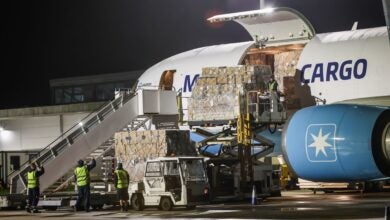 A cargo jet with light-blue engine trim being unloaded at night, with cargo door open.