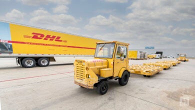 A yellow DHL tractor trailer and airport tug on a paved lot.