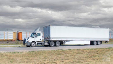 A white tractor-trailer on highway with a freight train in the background