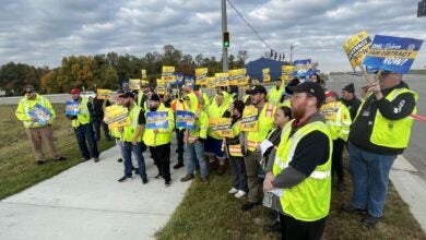 DHL workers wearing yellow vests and holding signs on a street corner picketing for a better contract.