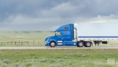 A blue tractor pulling a white trailer on a highway