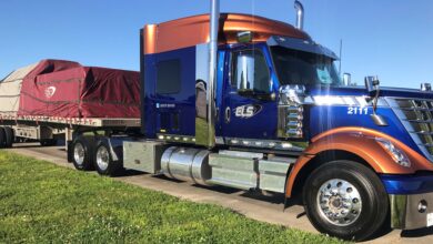 A blue ELS tractor with a covered load on a flatbed trailer