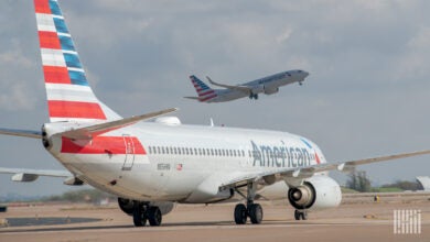 An American Airlines jet with American flag colors on the tail moves on airport taxiway.