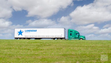 A green tractor pulling a white Landstar trailer